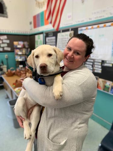 Lauren King of MWD in a classroom holding a yellow lab