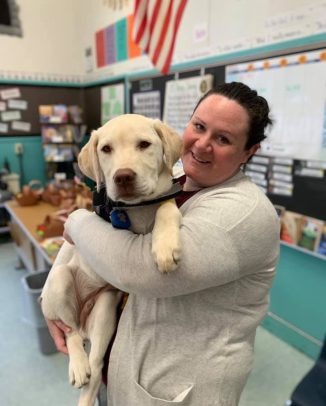 Lauren King of MWD in a classroom holding a yellow lab